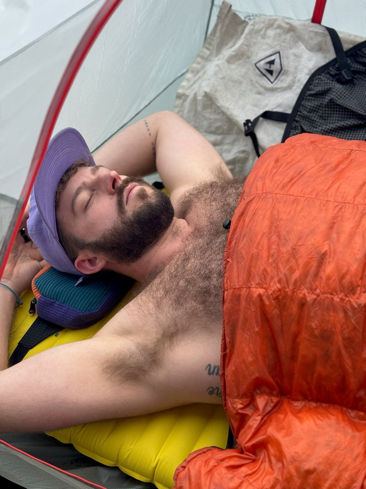 Justin sleeping in a tent under an orange quilt