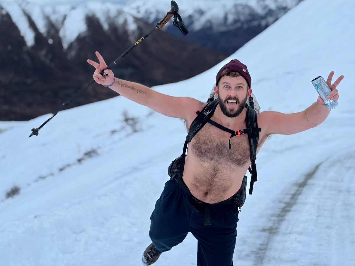Justin hiking shirtless through snow with a backpack and trekking poles